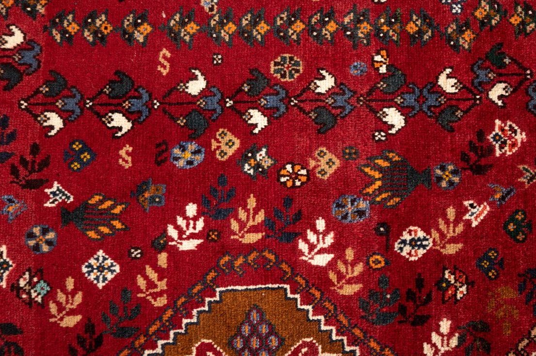 A Persian Qashqai carpet with a rich red and navy blue color scheme and central medallion motif.