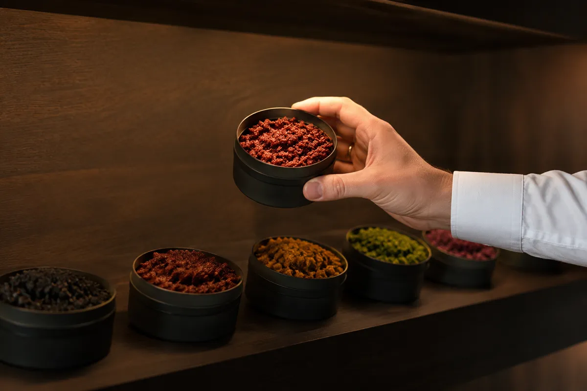 A row of open shisha tobacco tins on a dark shelf with one lifted clear to be chosen