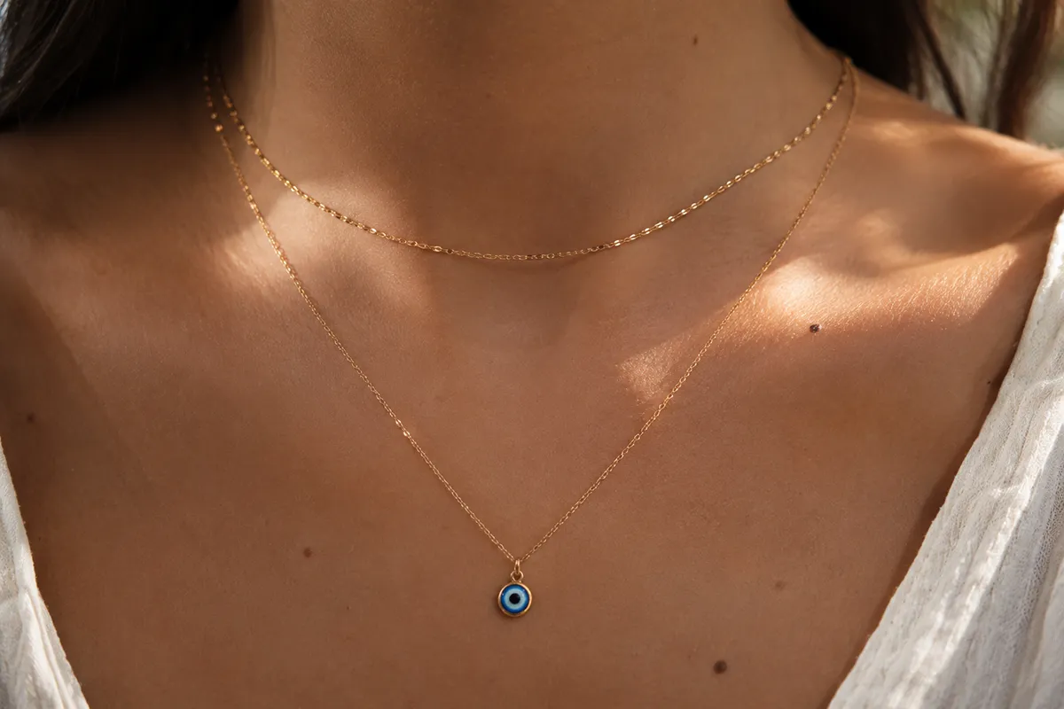 An evil eye necklace layered with other gold necklaces