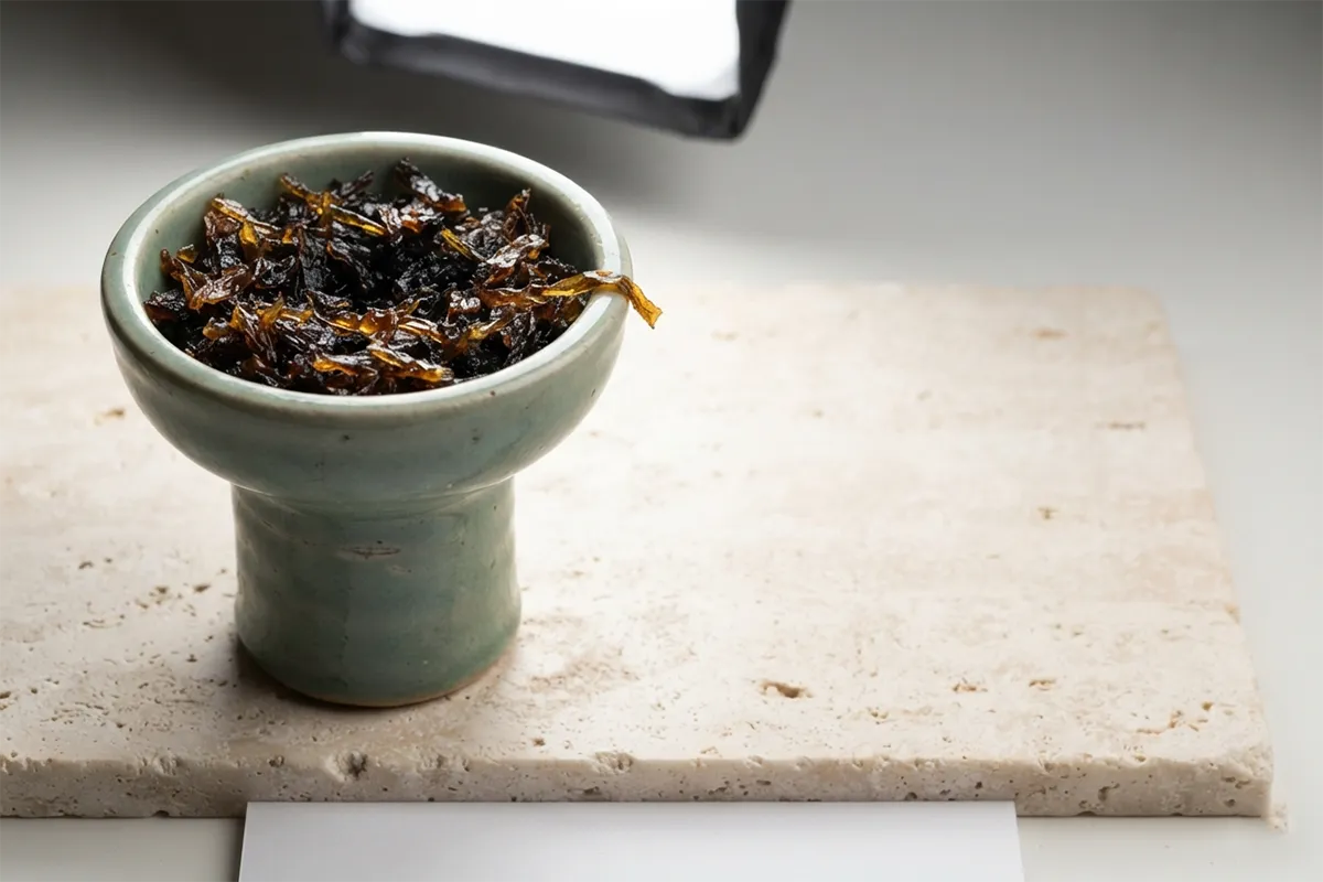 Macro detail of glossy shisha tobacco packed inside a glazed clay bowl on pale stone